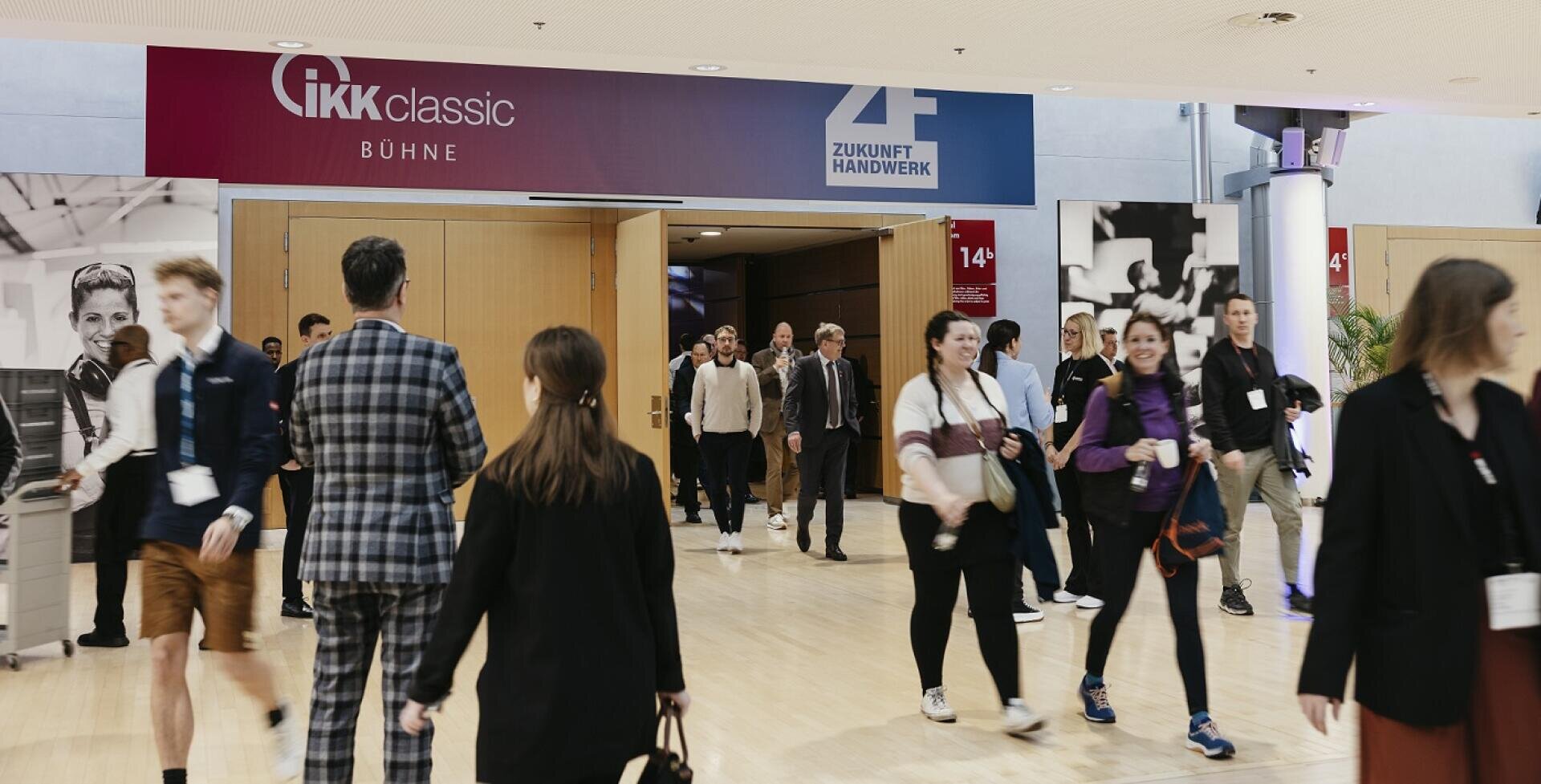 Eine Gruppe von Menschen geht durch weit geöffnete Türen in einen hellen Foyerbereich einer Konferenz oder Veranstaltung, über dem Transparente mit der Aufschrift IKK classic Bühne und Zukunft Handwerk hängen.