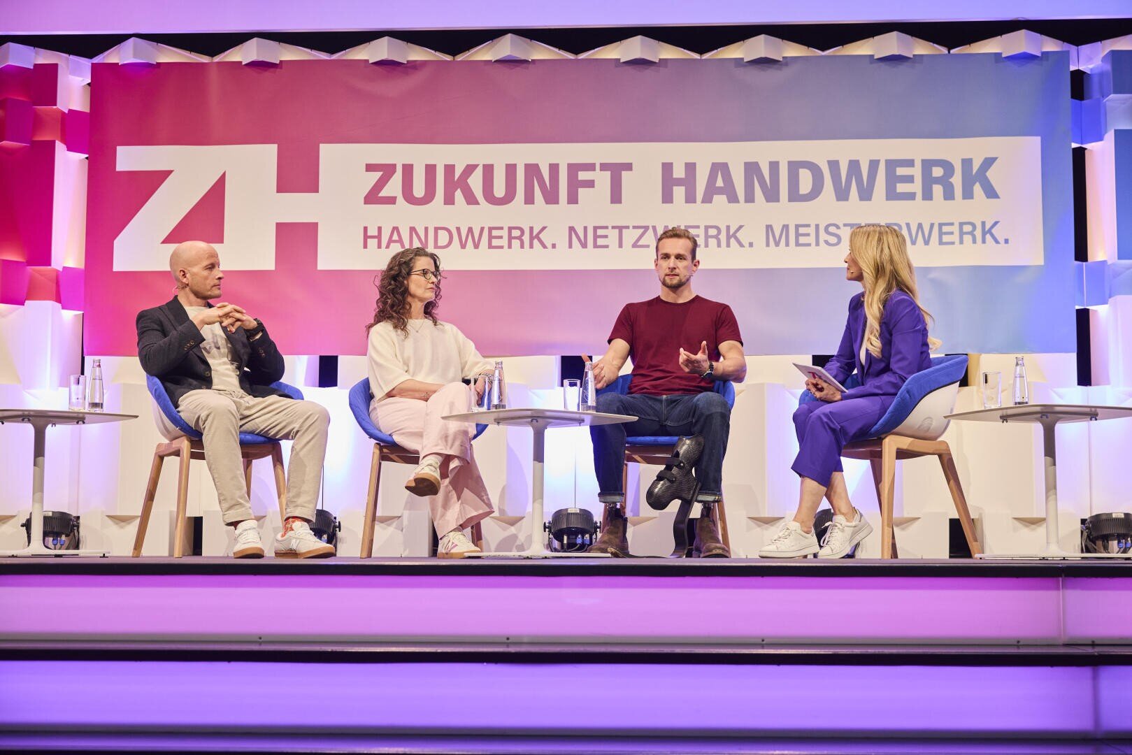 Vier Personen sitzen auf der Bühne und führen eine Podiumsdiskussion vor einem bunten Banner mit der Aufschrift Zukunft Handwerk - Handwerk. Netzwerk. Meisterwerk. Bei hellem Licht scheinen sie sich zu unterhalten.